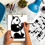 A person's hands sitting at a table with a pencil, finishing a detailed grid drawing puzzle of a panda by recreating designs from the instruction sheet next to the drawing.