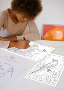 A woman coloring two detailed coloring pages of wild birds in their natural habitat, surrounded by trees and foliage.