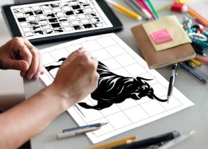 A person's hands finishing a grid drawing puzzle of a bull, copying the squares from the instruction sheet placed next to the drawing on the table.