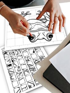 A woman completing a mystery grid puzzle drawing with a pencil, following an instruction sheet placed next to her drawing.