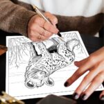 An adult woman's hands holding a pen, ready to color a detailed coloring page of an African spotted hyena.