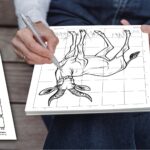 A man using a pen to complete a mystery grid drawing puzzle of an African klipspringer, following the grid instructions and copying squares from the template on a bench next to him.